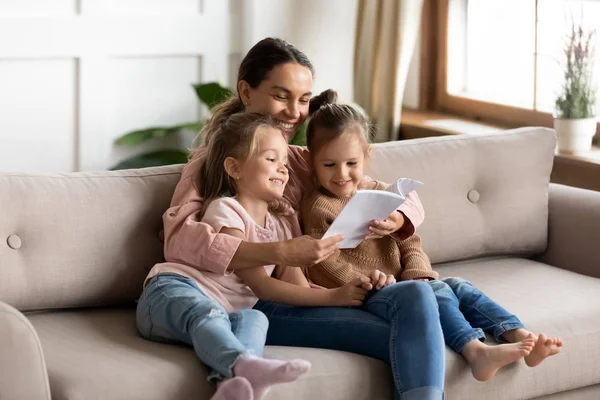 Gelukkige jonge moeder lees boek omarmen kleine kinderen dochters — Stockfoto