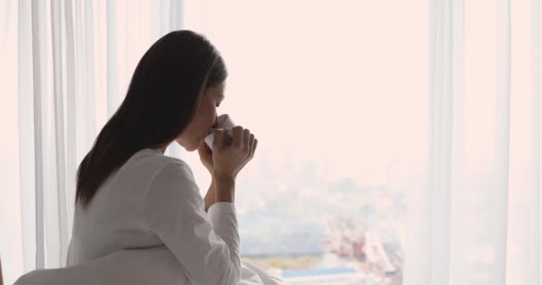 Feliz joven sentada en una acogedora cama bebiendo té — Vídeos de Stock