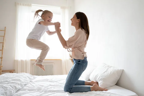 Cheerful mum play with active kid girl jump on bed — Stock Photo, Image