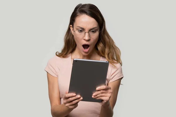 Шокована молода жінка в окулярах дивиться на екран планшетного комп'ютера — стокове фото