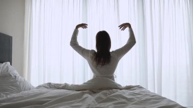 Genç kadın esneyerek uyanıyor, yatakta oturuyor, ağır çekimde.