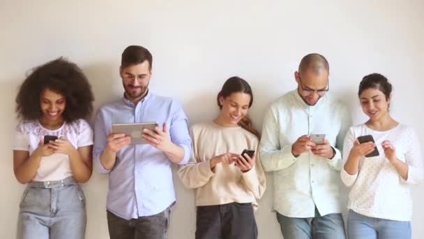 Multiracial sonriente grupo de jóvenes utilizando gadgets de pie en fila — Vídeo de stock