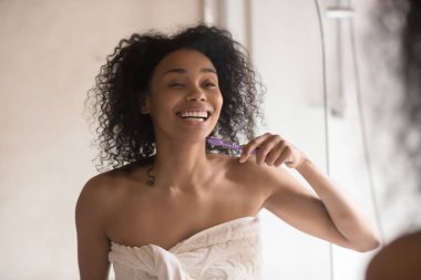 Gülümseyen melez kadın banyoda dişlerini fırçalıyor.