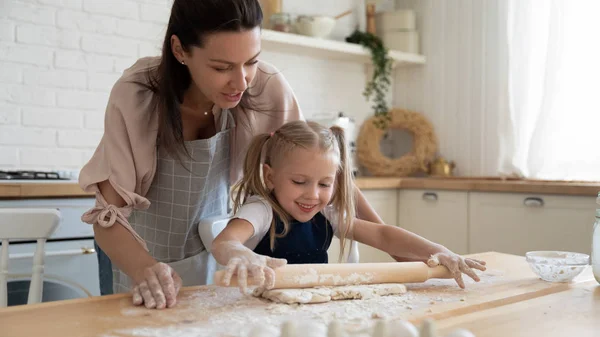 Happy mom teaching small child daughter rolling dough in kitchen — Stock Photo, Image