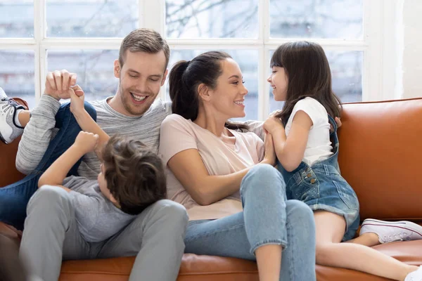 Happy parents playing with little kids relaxing on couch — ストック写真