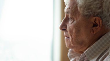 Pencereden dışarı bakan, anılarını hatırlayan düşünceli yaşlı bir adam..