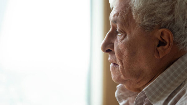 Pensive older man looking out of window, recollecting memories.