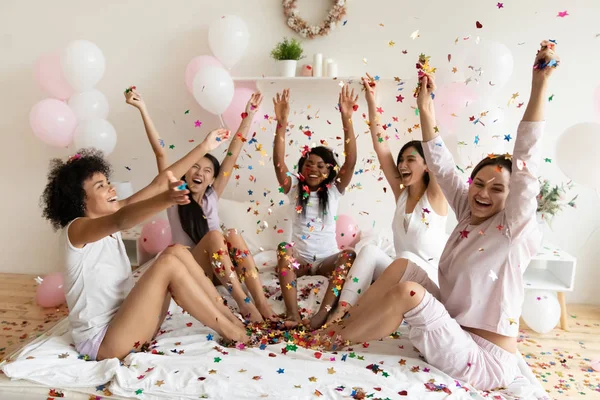 Happy ladies throw confetti up sit on bed celebrate party — Stock fotografie