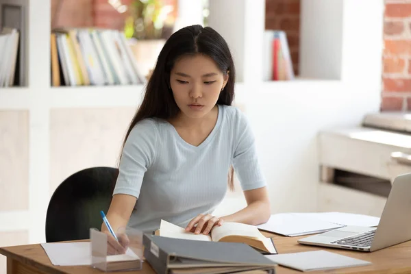 Концентрированная молодая азиатская студентка сидит за столом в библиотеке . — стоковое фото