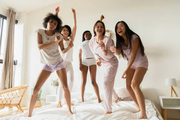 Lucu positif multirasial wanita menari di tempat tidur melihat kamera — Stok Foto