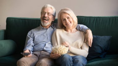 Evde oturup komedi izleyen olgun eşler.