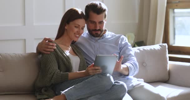 Счастливая взрослая пара смеется вместе с помощью планшетного компьютера на диване — стоковое видео