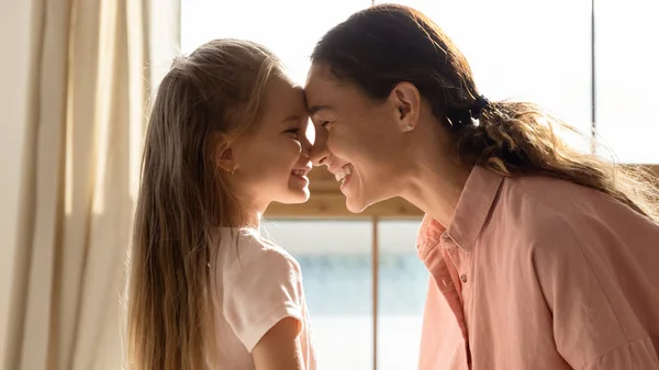 Glada mor och söt dotter vidrör näsor i soligt rum — Stockfoto