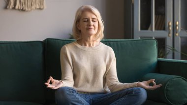 Huzurlu yaşlı kadın nilüfer pozisyonunda oturup evinde meditasyon yapıyor.