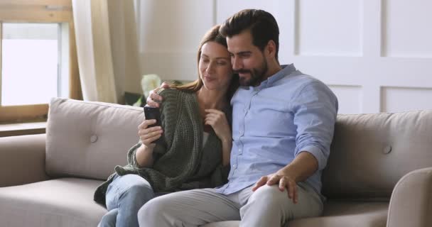 Casal feliz segurando smartphone usando aplicativos de mídia social no sofá — Vídeo de Stock