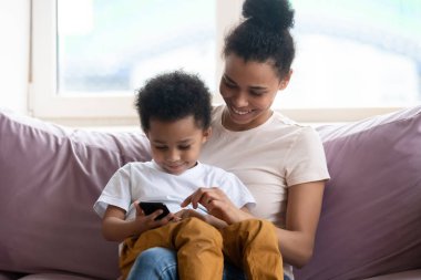 Mutlu Afrikalı Amerikalı anne küçük oğluyla akıllı telefonda oynuyor.