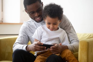 Genç Afrikalı Amerikalı baba küçük oğluyla cep telefonuyla oynuyor.