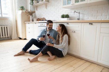 Romantik çift sıcak mutfak zemininde oturup şarap içerek konuşuyor.