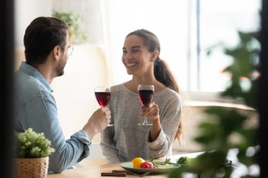 Gülümseyen bir çift kutlama yaparken ellerinde kadehlerle evde oturuyor.