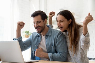 Laptop kullanan heyecanlı genç çift online galibiyeti kutluyor.