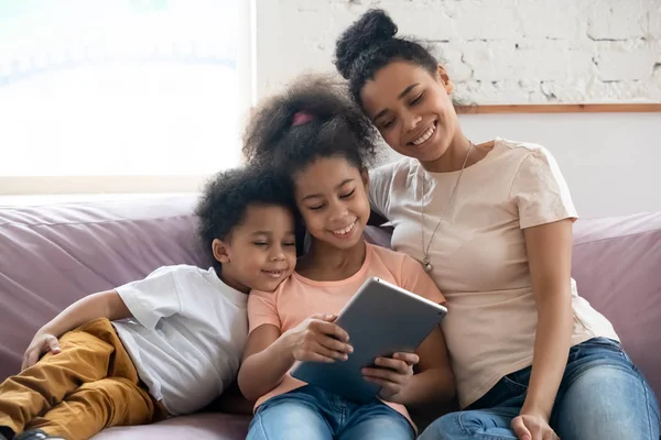 Heureuse maman biraciale et les petits enfants se détendre en utilisant une tablette — Photo