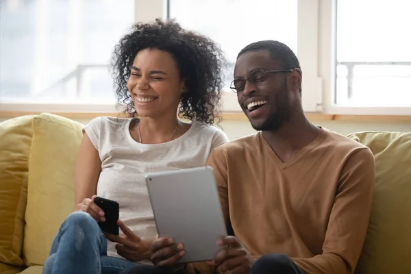 Aşırı neşeli Afrikalı Amerikalı çift tabletten komik videolar izlerken gülüyor. — Stok fotoğraf