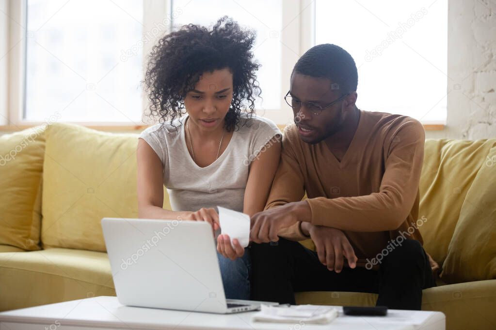 Biracial couple sit on couch managing finances paying bills
