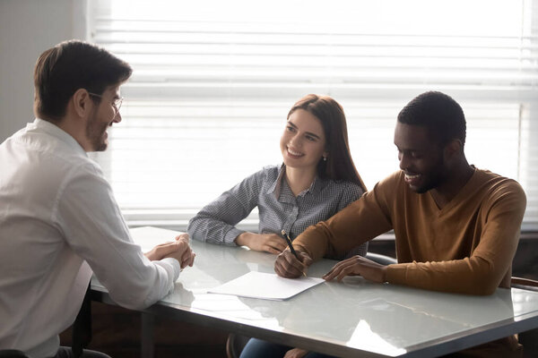 Excited multiethnic couple sign deal closing deal with realtor