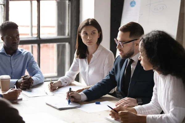 Empleados jóvenes de raza mixta concentrados escuchando a un director ejecutivo masculino confiado . — Foto de Stock