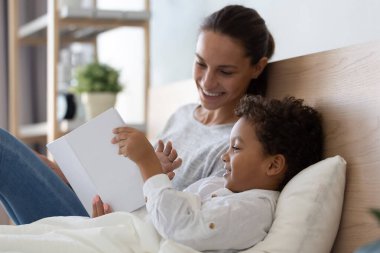 Karışık ırk ailesi yastıklarda uzanıp kitap tutuyorlar..