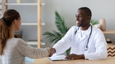 Sevimli Afro-Amerikan erkek doktor hastasıyla el sıkışıyor..
