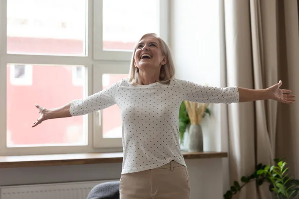 Mujer mayor de pie en la sala de estar manos extendidas se siente feliz —  Fotos de Stock