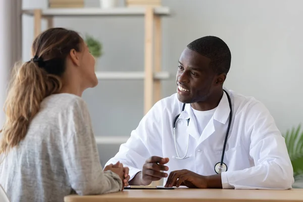 Leende ung kvinna besöker afrikansk amerikansk läkare. — Stockfoto