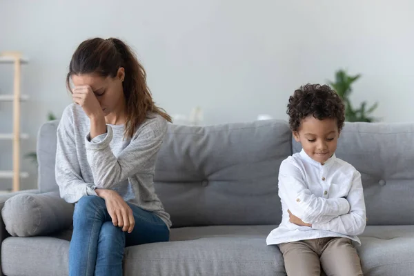 Frustrated upset woman sitting on couch aside unhappy little kid.