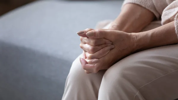 Mujer anciana sentada en el interior de las palmas dobladas en el regazo sensación de soledad — Foto de Stock