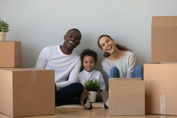 Overjoyed mixed race family sitting on floor near cardboard boxes.