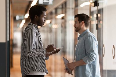 Çok ırklı meslektaşlar ofis koridorunda dikilip konuşuyorlar.