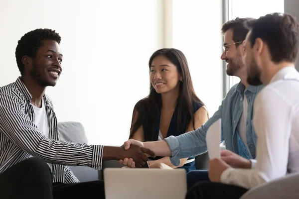 Socios multiétnicos sentados en el sofá estrechan las manos comienzan reunión del grupo — Foto de Stock