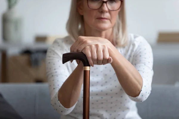 Vrouw van middelbare leeftijd, zittend op een bank met een stok in de hand — Stockfoto