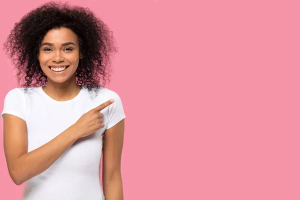 Smiling African American woman pointing finger at pink copy space — Stock Photo, Image