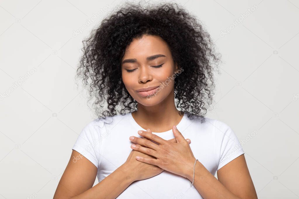Grateful hopeful African American woman holding hands on chest