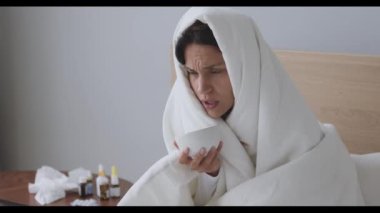 Battaniyeye sarılmış, yatakta oturan sağlıksız melez kız..