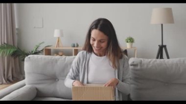 Şaşırmış genç bir kadın, internet siparişiyle karton kutu açıyor..