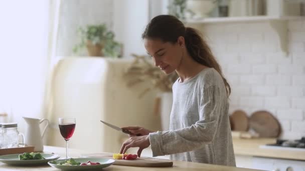 Счастливая молодая женщина режет свежие овощи для салата на кухне — стоковое видео