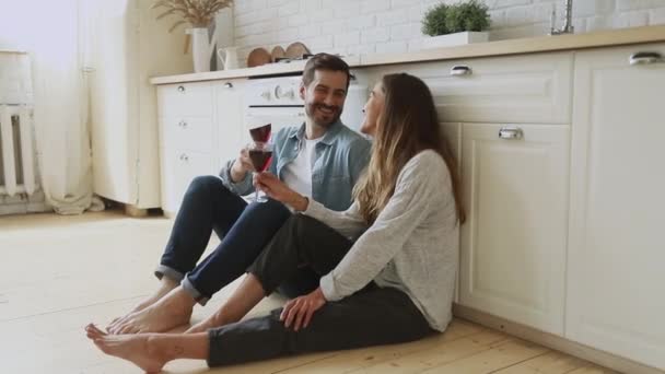 Ευτυχισμένο ζευγάρι κρατάει ποτήρια πίνει κρασί κάθεται στο πάτωμα της κουζίνας — Αρχείο Βίντεο