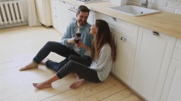 Milující pár sedět na podlaze kuchyně pít víno mluvit smích — Stock video