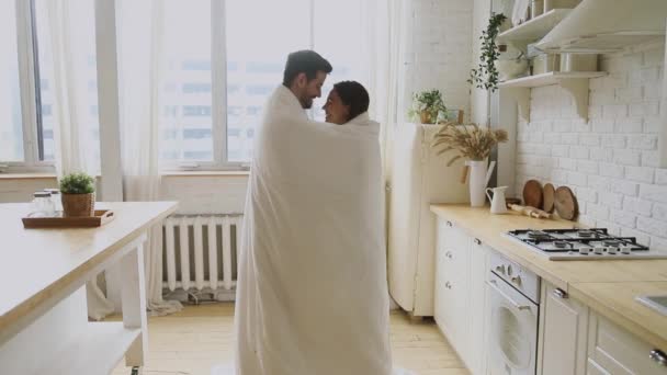 Feliz pareja romántica joven de pie en la cocina envuelta con manta — Vídeos de Stock