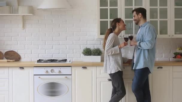 Happy romantic young couple holding glasses talking standing in kitchen — Stock Video