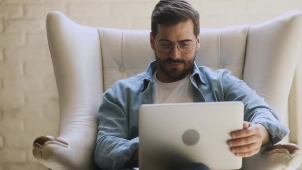 Jovem homem feliz sentar na cadeira usando laptop relaxante rindo — Vídeo de Stock