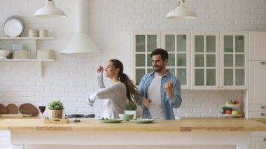 Genç, mutlu, aktif aile çifti mutfakta birlikte gülüp dans ediyor.
